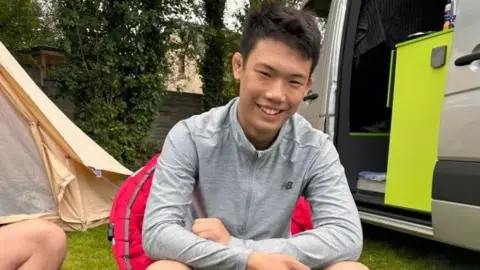 Phil Zhu smiling and sat in front of tent and campervan