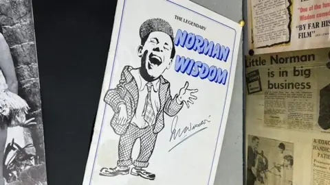 Play programme showing charicature of 'The legendary Norman Wisdom' amongst other 1950s newspaper clippings