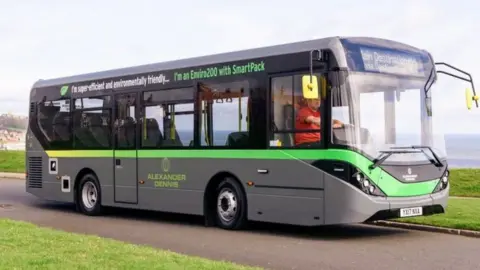 a grey electric bus with a green line and writing across it. It has an Alexander Dennis logo on the side.