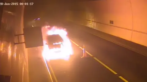 National Highways CCTV still image showing a car on fire inside a tunnel