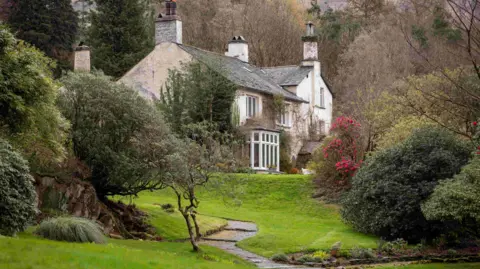 Supplied A narrow winding stone path leads to Rydal Mount, a two-storey white house with several chimneys. It is surrounded by grassland and lots of trees and shrubs. 