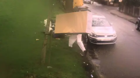 Brent Council's photograph of Mr Abbas trying to dump a bed on a grassy roadside. The man carries a bed base and his legs can be seen beneath it.