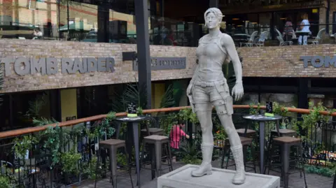 The nine foot (2.74m) statue of Lara Croft in a room with signs on the wall that says TOMB RAIDER