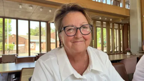 Woman in white shirt and black-ruimmed glasses smiles aT camera