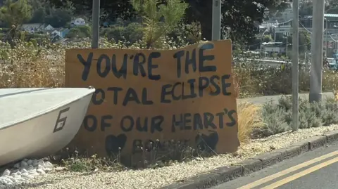 BBC A cardboard sign welcoming visitors to Mumbles reads "You're the Total Eclipse of our hearts Bonnie", referencing the singer's 1982 hit.