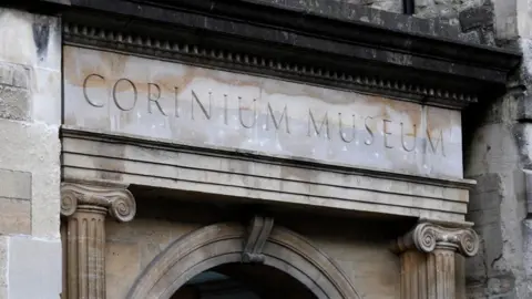 An exterior view of the Corinum Museum, showing a stone arch and the museum name carved in stone above