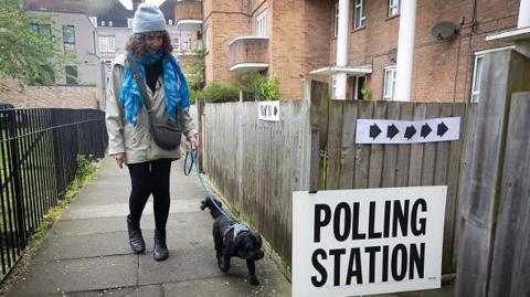 Woman walking a dog near a polling station sign