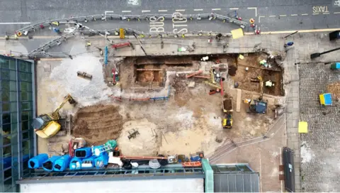 The remains of a Roman road can be seen by the side of a road and a bus stop in Manchester city centre.