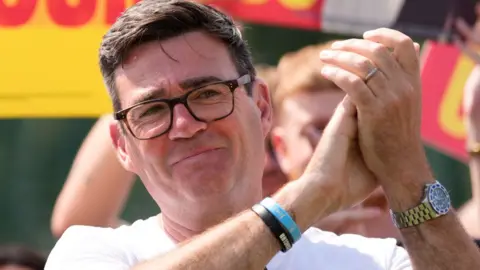 Andy Burnham claps his hands and smiles as he looks past the camera at a Labour Party rally