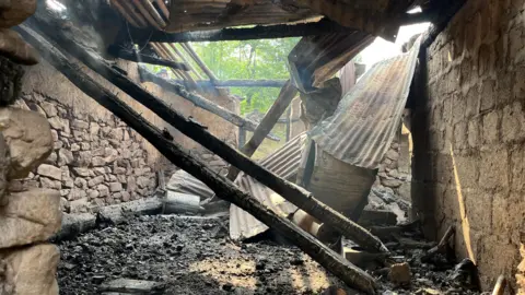 The inside of a ruined stone home, with the tin roof caved in