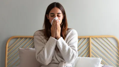 Getty Images Young woman blows her nose in bed 