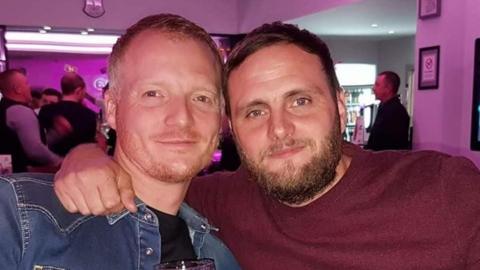 Two men sharing an embrace for a photo in a bar