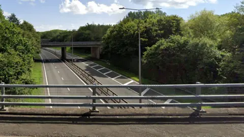 Google A view of the A442 carriageway from a bridge at Wombridge. The road is clear in both directions with trees either side of it.