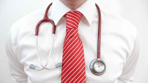A doctor's torso close up with a red tie and stethoscope 