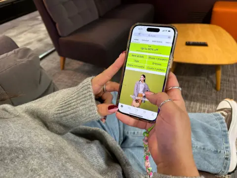 A woman's hand holding a phone. The ASOS app is open on the screen