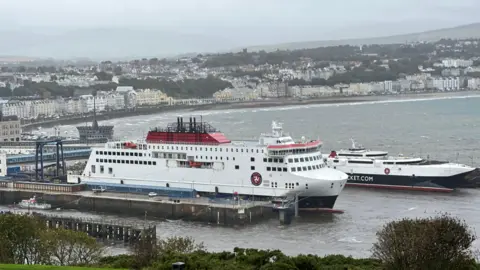 The Manxman and Manannan in Douglas Harbour on a rainy, cloudy day with buildings on Douglas seafront in the background. 