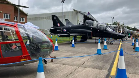 Aircraft taking part in Cosford air show in 2024 are on the ground and surrounded by blue and white cones and blue cordons at the air base.