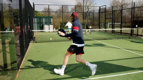 AFP/Getty Images Stock images shows two teams of two playing against each other on a padel court. There is a net in the centre and they are all holding racquets. Around the outside is a glass/plastic wall. 
