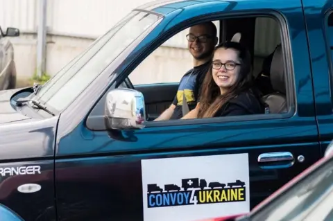 Louis Mitchell Kayleigh Jones looking out of the window of a dark-coloured vehicle, with the words Convoy 4 Ukraine on the door and her partner, Josh Katihrob, sitting in the driver's seat