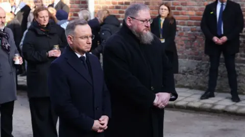 Getty Images Polish President Andrzej Duda and Piotr Cywinski, Auschwitz Museum director, pay homage at 'The Death Wall' during the 80th anniversary of the liberation of Auschwitz at Memorial and Museum Auschwitz-Birkenau former Nazi-German concentration and extermination camp