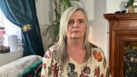 Mark Ansell/BBC Lorna Squires in her front room. She is wearing a cream blouse with colourful artwork on.