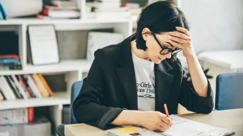 Getty Images Teacher at a desk with head in hands