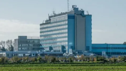 The outside of Boston Pilgrim Hospital, with fields, trees and sky surrounding the glass windows and tall building