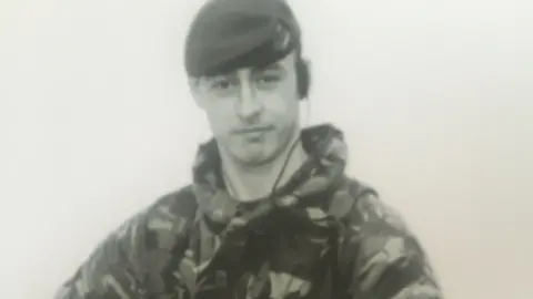 Warwickshire Police A man is wearing camouflage uniform and a military hat, while holding a rifle. 