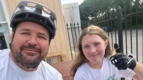 Children’s Hospice South West Dad Ian Nash and his daughter Charlie on their bike ride challenge. Mr Nash is wearing a bike helmet.