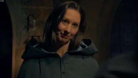 Rachel in the turret wearing her green traitor's cloak and a suspicious and unimpressed look