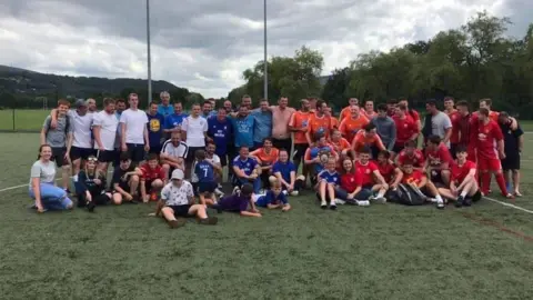 Chloe Cooper A wide image of a large group of men and children stood on a rugby field looking at the camera. 
