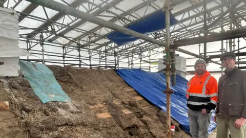 MNH Scaffolding surrounds the roof, two men stand on the roof smiling.