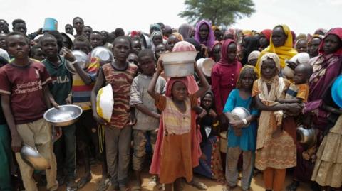 Sudanese children line up to receive rice portions from Red Cross volunteers