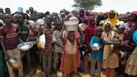 Reuters Sudanese children line up to receive rice portions from Red Cross volunteers