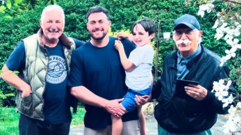 Arran Campolucci-Bordi is pictured holding his son and standing next to his father and grandfather in a garden. 