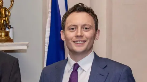 PA Media A man with dark hair smiling at the camera