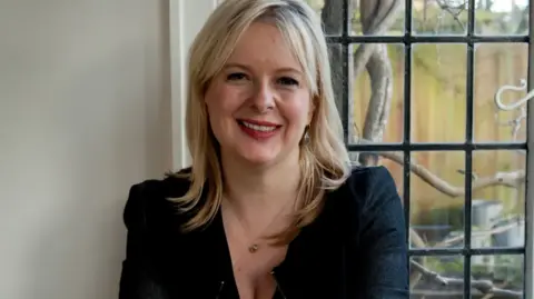 Pearson poses for the photo, smiling, in front of a window