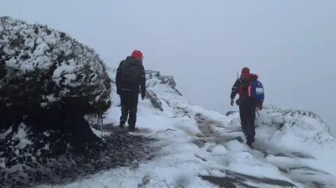 Glossop Mountain Rescue Two people in waterproof clothing looking across misty, snow covered moorland