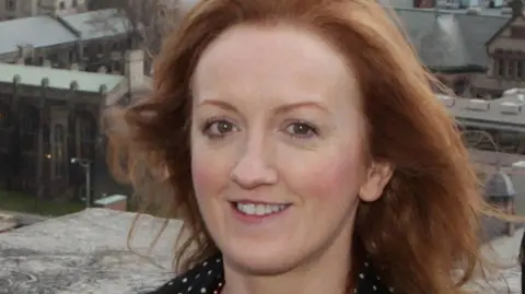 Edinburgh Festival Fringe chief executive Shona McCarthy, who has reddish hair, looking into the camera on a rooftop in Edinburgh with the Old Town as a backdrop.