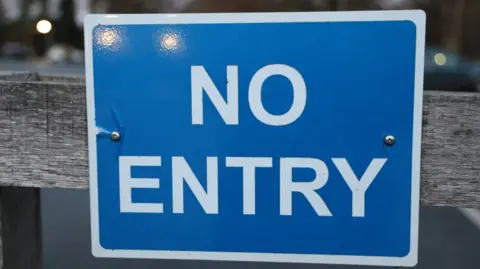 A blue square no entry sign has been pinned to a wooden fence.