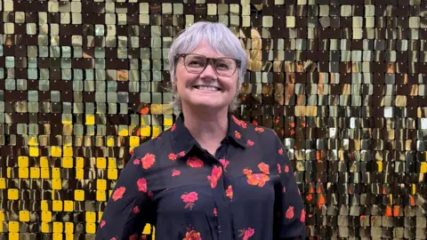 BBC Yvonne Hughes smiles in front of a mosaic background