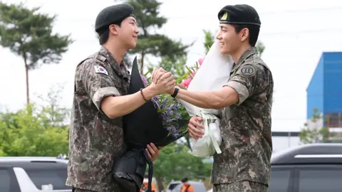 RM, left, dressed in military uniform, shakes hands with V, right, also in military uniform