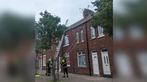 RSPCA Firefighters erecting a ladder to free a bird trapped in a TV aerial on top of a terraced house roof