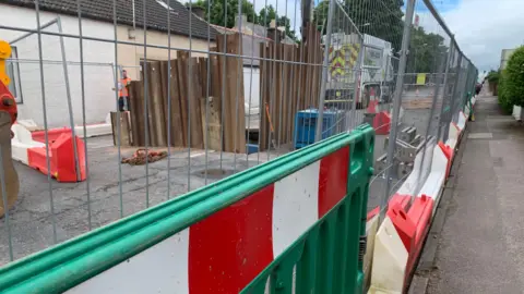A fenced-off area with vehicles inside it and metal bars sticking up out of a large hole