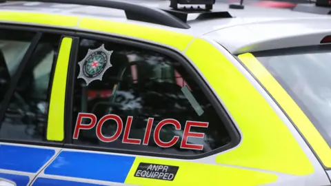 A yellow and blue police car with tinted windows, a black roof and 'police' written in red writing up the back window.