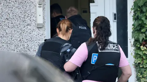 Four police officers are pictured entering a house.