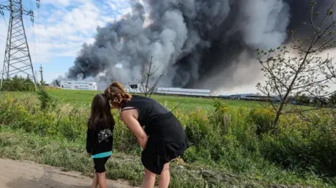 People watch as smoke rises above a Wildberries facility following a reported Ukrainian drone strike at the Koledino Industrial Park near Podolsk in Russia on 16 August.