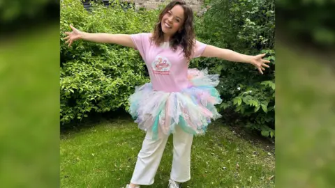 Flamingo Chicks Evie Pickerill standing in a garden with her arms outstretched, wearing a pastel colour tutu