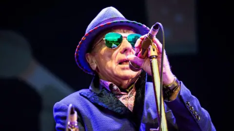 Getty Images Sir Van Morrison singing into microphone, wearing a hat and sunglasses 