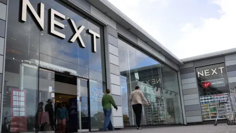 A Next store is seen with the logo looming large over passers-by as they walk outside the storefront on a sunny-cloudy day in Basildon in October.